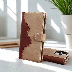 Könnte beinhalten: Zweifarbiges Handy-Etui aus braunem und beigem Leder. Das Etui hat ein wellenförmiges Design auf der linken Seite und einen Magnetverschluss. Daneben liegt ein passendes Handy-Etui. Die Etuis dienen zum Schutz des Telefons.