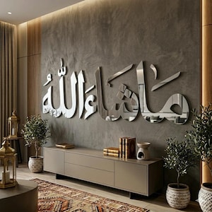 Peut inclure: Une grande pièce d'art mural réfléchissante de couleur argentée présentant une calligraphie arabe qui se lit Mashallah. L'écriture est montée sur un mur texturé gris foncé au-dessus d'un long meuble bas rectangulaire à la finition mate.