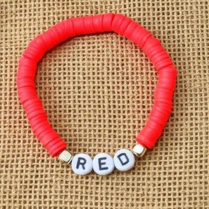 Könnte beinhalten: Ein leuchtend rotes Armband mit dem Wort "RED" in weißen Buchstabenperlen. Das Armband besteht aus kleinen, flachen, runden roten Perlen und liegt auf einem strukturierten, beigefarbenen Hintergrund.