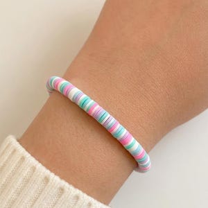 May include: A stretch bracelet composed of small, flat, circular clay beads in a repeating pattern of pastel pink, light blue, white, and mint green. The beads are arranged in a single strand, creating a colorful, uniform, and lightweight accessory.