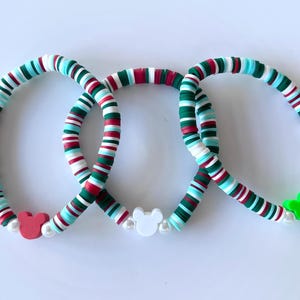 May include: Three colorful bracelets with a festive design. Each bracelet features a pattern of red, white, green, and turquoise disc-shaped beads. The bracelets are adorned with Mickey Mouse-shaped charms and white pearl beads.
