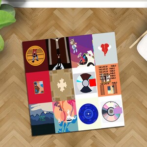 May include: A square art print featuring a collage of album covers and designs. The artwork includes various colors and graphics, including a bear, a broken heart, and the text "THE LIFE OF PABLO". The print is displayed on a wooden floor.