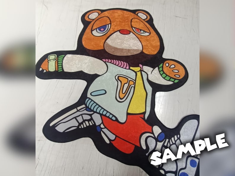 May include: A colorful rug featuring a cartoon bear with a sad expression. The bear is wearing a jacket with a "T" on it, and the design incorporates elements of a skeleton. The rug is approximately 48 inches long.