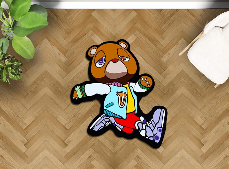 May include: A brown bear-shaped rug with a cartoon design. The bear wears a blue jacket, red pants, and purple sneakers. The rug has a black border and is placed on a wooden floor.