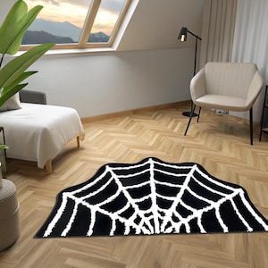 Op de afbeelding: Een zwart-wit vloerkleed met een spinnenwebontwerp. Het kleed is gevormd als een spinnenweb en heeft een pluche textuur.