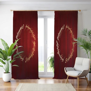 May include: Burgundy-coloured curtain panels with a gold-coloured ring design. The design features script around the oval shape. The curtains are hanging in front of a window, with plants and a chair visible in the room.