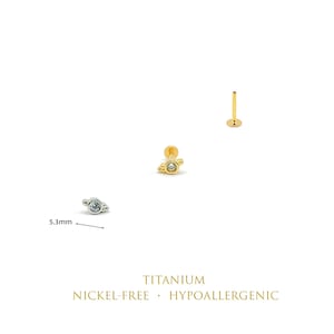 May include: Three flat back stud earrings featuring a planet-shaped design with a central clear stone. One silver-tone and two gold-tone studs are shown, with a 5.3mm measurement indicated for the silver stud. Text reads: TITANIUM NICKEL-FREE HYPOALLERGENIC.