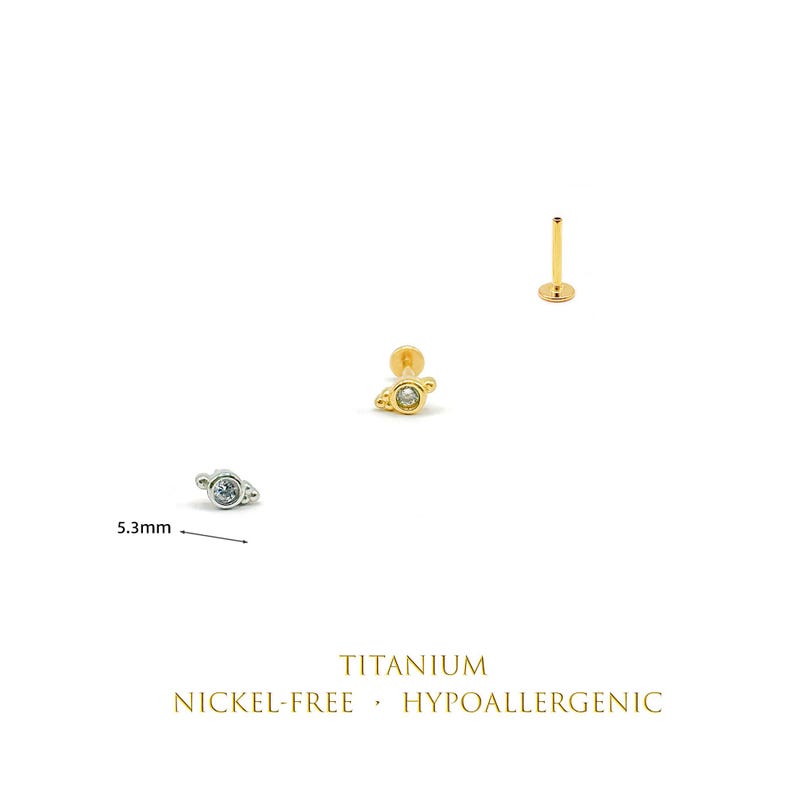 May include: Three flat back stud earrings featuring a planet-shaped design with a central clear stone. One silver-tone and two gold-tone studs are shown, with a 5.3mm measurement indicated for the silver stud. Text reads: TITANIUM NICKEL-FREE HYPOALLERGENIC.