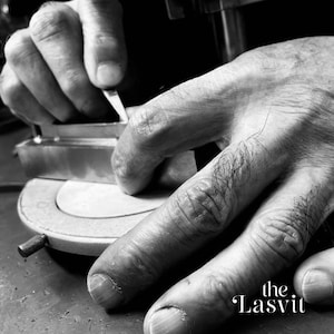 May include: A black and white close-up of a metal tool being held against a circular base. The metal object has a rectangular shape and is being manipulated by fingers. The text "the Lasvit" is printed in the lower right corner of the image.
