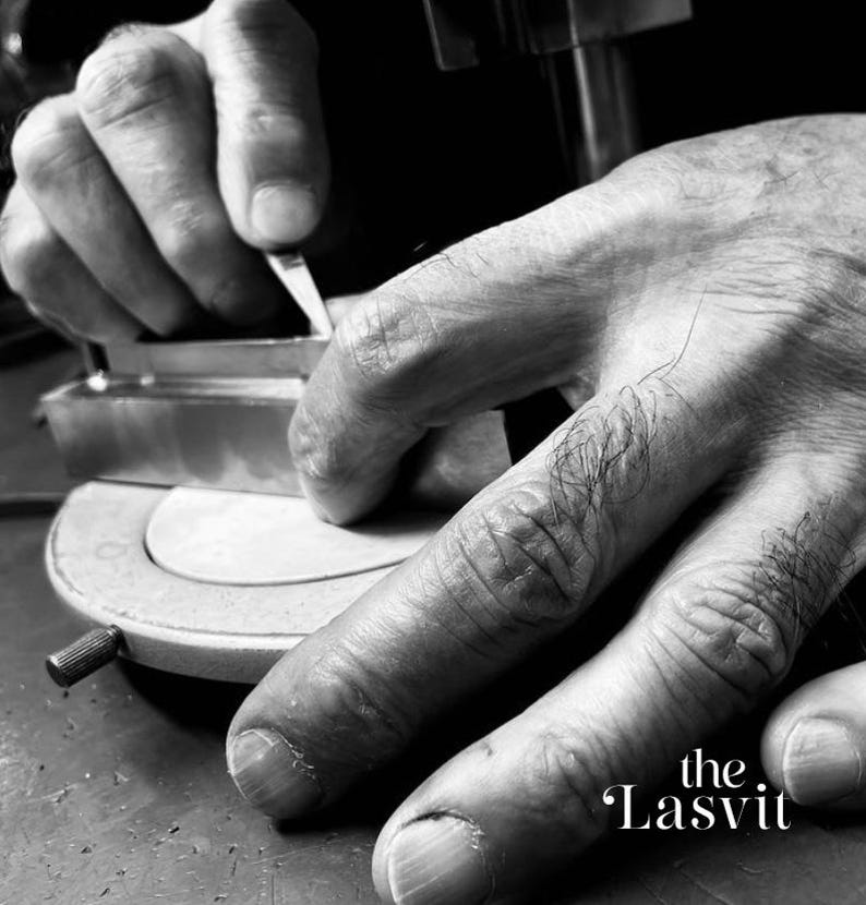 May include: A black and white close-up of a metal tool being held against a circular base. The metal object has a rectangular shape and is being manipulated by fingers. The text "the Lasvit" is printed in the lower right corner of the image.