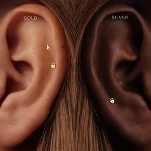 May include: Two gold-toned ear studs shaped like a key and a heart-shaped padlock are worn on one ear, while a single silver-toned heart-shaped padlock ear stud is worn on the other ear. The text GOLD and SILVER labels the respective sides.
