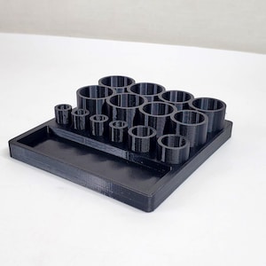 May include: Black plastic organizer with multiple circular compartments of varying sizes. The organizer has a rectangular tray in the front.