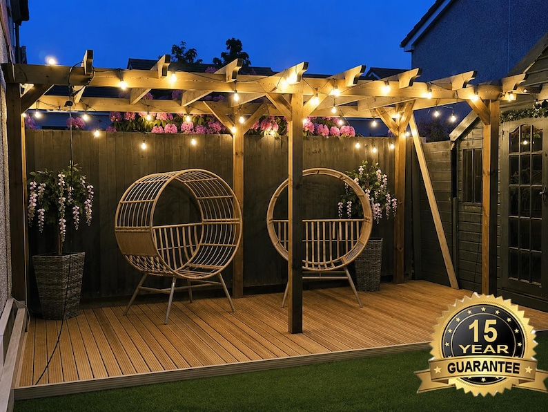 May include: A wooden pergola structure featuring a string of warm glowing lights, two circular rattan-style chairs, and a wooden deck floor. A gold badge in the corner displays the text 15 YEAR GUARANTEE, indicating a long-term product warranty.