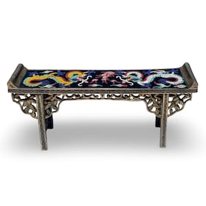 Op de afbeelding: Een rechthoekige displaystandaard met een zwart bovenoppervlak versierd met twee kleurrijke draken in geel, wit en blauw. De standaard heeft een donker, verweerd metalen frame met ingewikkeld opengewerkt houtsnijwerk op de poten.