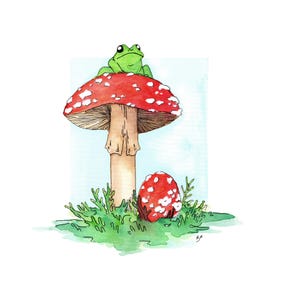 May include: A green frog sits on top of a red and white mushroom with white spots. A smaller red and white mushroom with white spots is on the ground next to the larger mushroom. Both mushrooms are surrounded by green grass.