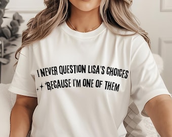 May include: White crew neck t-shirt with the text "I NEVER QUESTION LISA'S CHOICES + BECAUSE I'M ONE OF THEM" in black. The shirt is worn with light blue ripped jeans. The overall theme is casual wear.