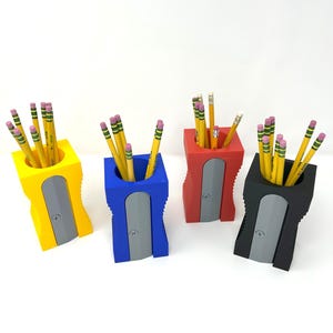 May include: Four pencil holders with built-in pencil sharpeners. The holders are yellow, blue, red, and black. Each holder has a row of pencils inside.