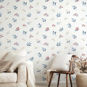 Peut inclure: Mur blanc avec un motif répété de feuilles bleues, de baies rouges et de petites fleurs blanches. Un canapé blanc avec des coussins et une chaise en bois avec un coussin blanc sont devant le mur. Un panier tressé avec des plantes séchées est à côté de la chaise.