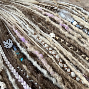May include: A close-up of a set of brown, blonde, and white synthetic dreadlocks with various embellishments, including feathers, beads, and charms.