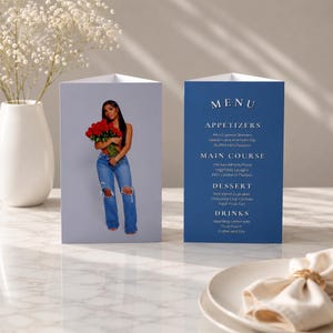 Peut inclure: Un menu pliable à trois volets présentant une photographie d'une personne tenant un bouquet de roses rouges sur un panneau et un menu imprimé avec des sections pour les entrées, plats, desserts et boissons sur l'autre panneau.