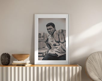 Puede incluir: Impresión enmarcada en blanco y negro de Muhammad Ali boxeando. La imagen muestra a Ali en una postura de boxeo con un horizonte urbano de fondo. La impresión se exhibe en un mueble de madera con objetos decorativos.