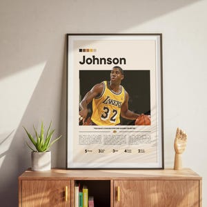 May include: Framed poster featuring a basketball player in a yellow Lakers jersey with the number 32. The poster has the name "Johnson" in bold letters and includes text at the bottom. The poster is displayed on a wooden cabinet.