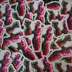 May include: A pile of stickers featuring a pink and green illustration of a character in a futuristic suit. The character is holding a large weapon.