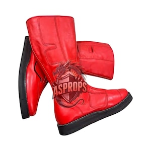 Puede incluir: Botas de cuero rojo brillante con suela negra. Las botas son de media caña y tienen la punta redondeada. También se ve un accesorio de cuero rojo a juego. Las botas tienen el texto "ASPROPS".