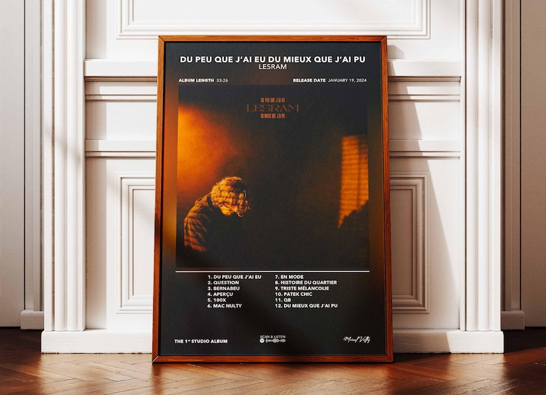 May include: Framed poster with the text "DU PEU QUE J'AI EU DU MIEUX QUE J'AI PU" and "LESRAM". The album art features a person in silhouette against an orange and black background. The poster is in a brown wooden frame.