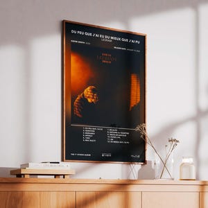 May include: Framed poster with the text "DU PEU QUE J'AI EU DU MIEUX QUE J'AI PU" and the artist's name, LESRAM. The poster features a dark, moody image with an orange and black color scheme. The album's tracklist is listed at the bottom.