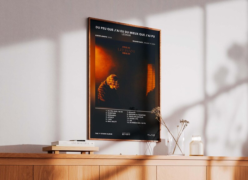 May include: Framed poster with the text "DU PEU QUE J'AI EU DU MIEUX QUE J'AI PU" and the artist's name, LESRAM. The poster features a dark, moody image with an orange and black color scheme. The album's tracklist is listed at the bottom.