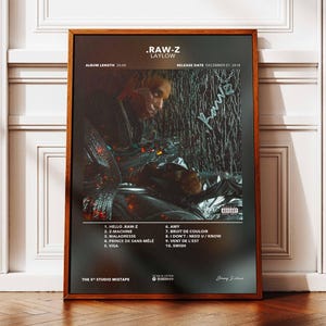 May include: A framed poster for the album ".RAW-Z LAYLOW" with a dark, moody aesthetic. The album art features a person in a reflective outfit. The poster includes the album length, release date, and tracklist.