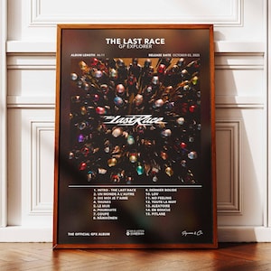 Peut inclure: Affiche encadrée de l'album "The Last Race", avec un fond sombre et des formes abstraites colorées. L'affiche comprend le titre de l'album, la liste des titres et la date de sortie, présentée dans un cadre en bois.