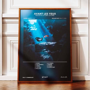 Peut inclure: Affiche encadrée avec le texte "AVANT LES YEUX" et les noms des artistes. L'œuvre présente une scène sous-marine bleu foncé avec des formes abstraites et la liste des titres de l'album. Le cadre est de couleur marron chaud.