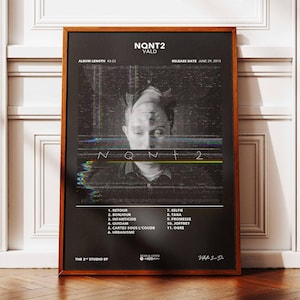 May include: Framed poster with a dark background featuring the text "NQNT2 VALD" and a distorted image of a person's face. The poster includes a tracklist and album details. The frame is a warm brown color.
