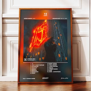 May include: A framed poster with a dark, stylized image of a person in front of a skyscraper with a fiery red design. The poster includes the album title "15 AMK", tracklist, and release date.
