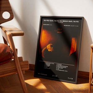 May include: A framed poster with the text "DU PEU QUE J'AI EU DU MIEUX QUE J'AI PU" and "LESRAM" in white font. The poster has a dark background with orange and yellow hues. The album's tracklist is listed at the bottom.