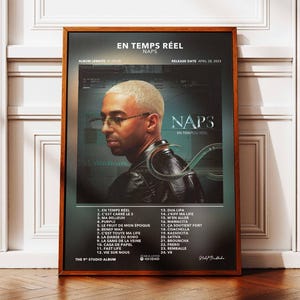 Peut inclure: Affiche encadrée de l'album "En Temps Réel" de Naps. L'œuvre présente un portrait de l'artiste, portant des lunettes et un blouson en cuir, sur fond sombre. Le titre de l'album et la liste des titres sont visibles.