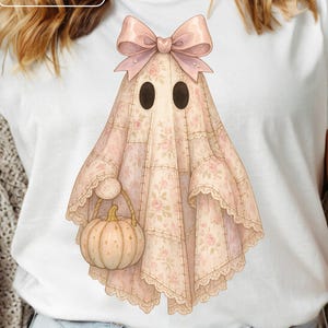 May include: White t-shirt featuring a watercolor illustration of a ghost. The ghost is draped in a pink floral patterned sheet, has a bow, and carries a pumpkin. The words "Digital Download" are in the upper left corner.