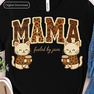 Peut inclure: T-shirt noir avec le mot "MAMA" dans un motif léopard marron. Deux chats de dessin animé portant des pulls à imprimé léopard tiennent des tasses à café. Le texte "fueled by java" est en dessous.