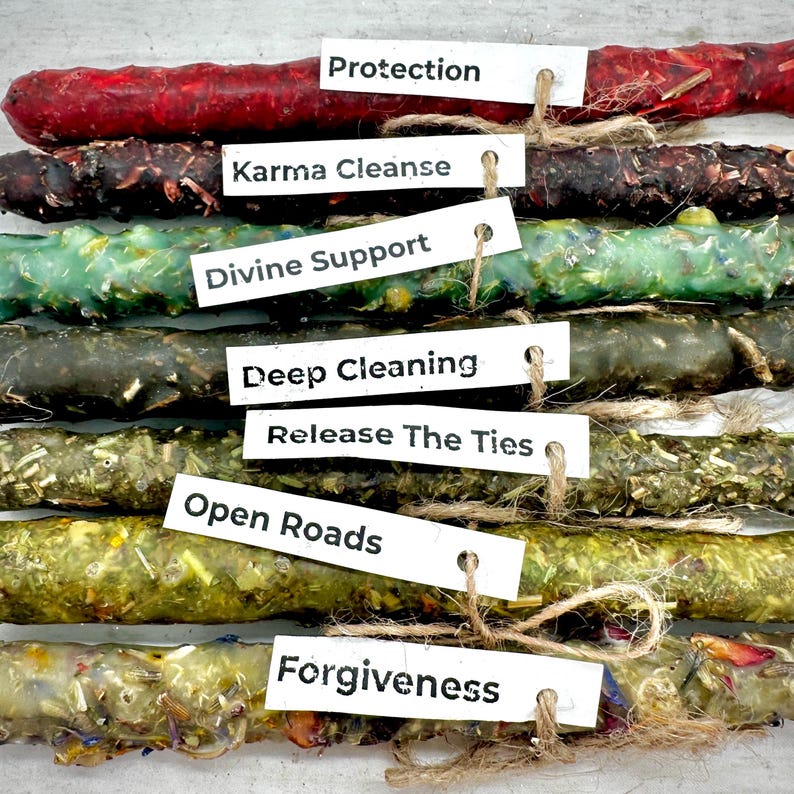 May include: An assortment of colorful, handcrafted candles with attached tags. The tags read "Protection," "Karma Cleanse," "Divine Support," "Deep Cleaning," "Release The Ties," "Open Roads," and "Forgiveness." The candles are various colors and textures.