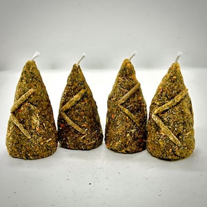 Può includere: Quattro candele a forma di cono con una superficie strutturata verde e marrone. Ogni candela ha uno stoppino bianco in cima ed è decorata con accenti chiari incrociati. Le candele sono disposte su una superficie bianca.