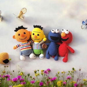 May include: Crocheted Sesame Street character dolls, including Bert, Ernie, Cookie Monster, and Elmo, are displayed against a white background. The dolls are in various colors, with details like striped shirts and smiling faces. Butterflies and colorful flowers add to the whimsical scene.