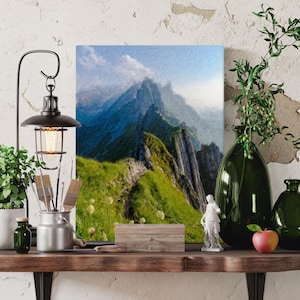 Op de afbeelding: Een schilderij van een bergketen met een kronkelend pad dat naar de top leidt. De bergen zijn diepblauwgroen en het pad is omzoomd met groen gras. De lucht is lichtblauw met witte wolken.