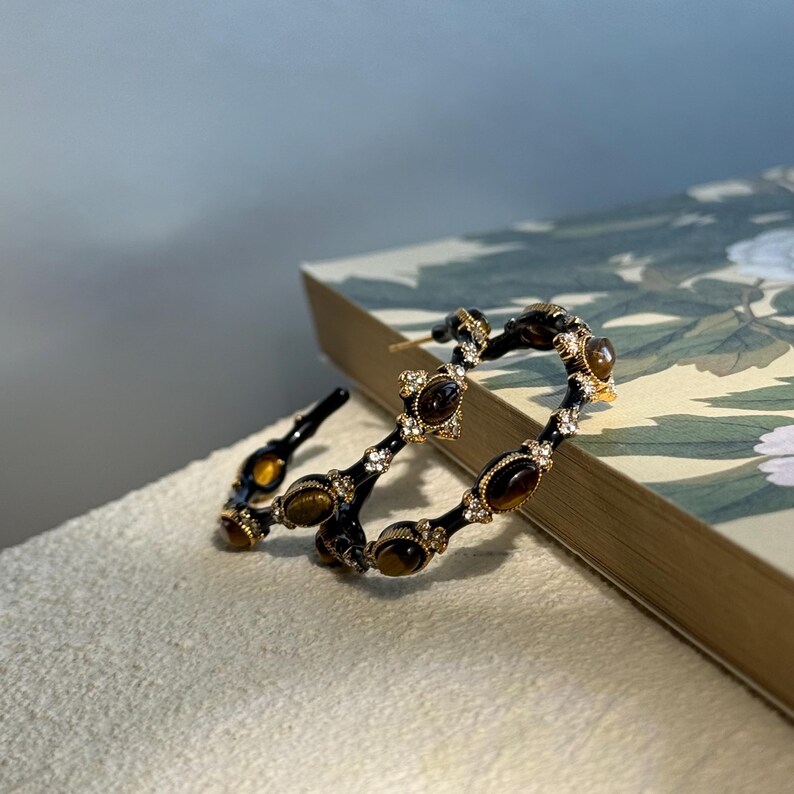 Angled light view of tiger’s eye rhinestone hoop earrings reflecting glossy gold texture and gemstone shimmer