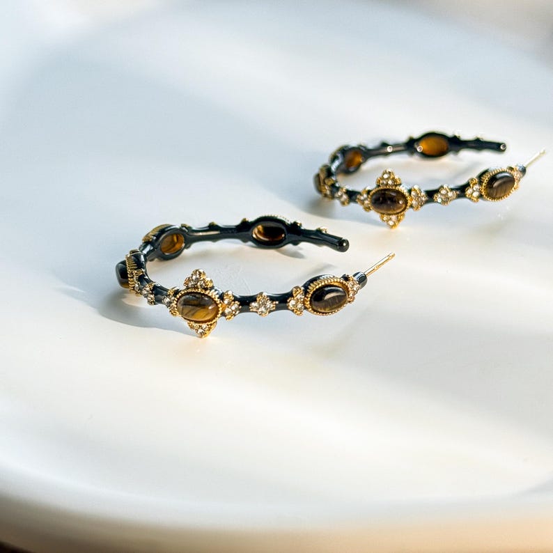 Pair of gold tone bamboo hoop earrings with tiger’s eye and rhinestones laid flat to show circular shape and textured metal design