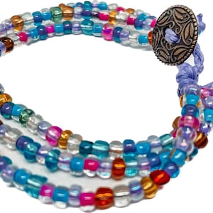 May include: Multi-strand beaded bracelet with a silver charm and purple tassel. The bracelet features a variety of colors including blue, green, pink, and gold.