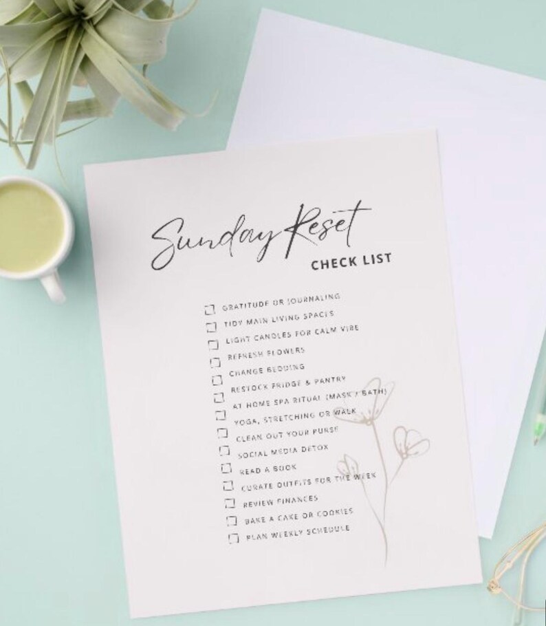 May include: A white checklist titled "Sunday Reset" with a handwritten font. The checklist includes items like "Gratitude or Journaling" and "Tidy Main Living Spaces." A cup of green liquid and a plant are in the background.