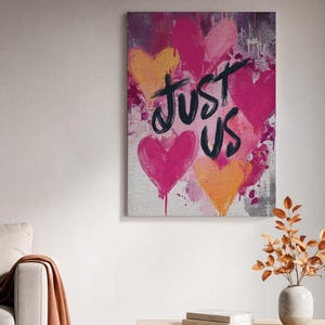 Puede incluir: Impresión artística en lienzo con un diseño vibrante de corazones rosas y naranjas sobre un fondo texturizado. Las palabras "JUST US" están escritas en escritura negra, agregando un toque personal a la obra de arte. Decoración de pared romántica y moderna.
