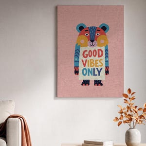 Puede incluir: Impresión en lienzo colorida con un oso de dibujos animados y el texto "GOOD VIBES ONLY". El oso tiene un esquema de color azul, rojo, amarillo y naranja. El fondo es de color rosa claro.